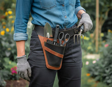 gardening tool pouch belt. The black and brown leather pouch contains a trowel, scissors, and a hand fork, and the person is wearing gray gloves.