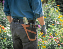A person viewed from behind wearing a gardening tool belt with a trowel, hand tools, and a small container