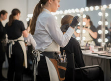 A makeup artist in black brown leather with a brush pouch stands