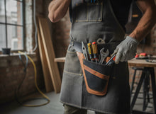 dark black brown tool roll with a brown leather tool pouch filled with hand tools, standing in a workshop