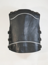 Black leather motorcycle vest shown from the back, featuring silver metal studs, buckle straps on the sides, and curved silver piping details, photographed against a plain white background.