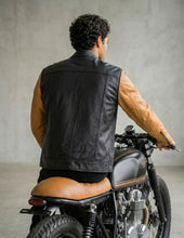 Man sitting on a motorcycle wearing a black and tan leather jacket.
