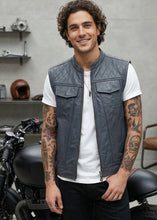 Man wearing a gray quilted leather vest over a white shirt, standing next to a motorcycle.