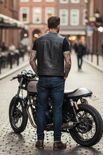 Back view of man wearing genuine black leather motorcycle vest while standing near bike — classic biker outfit.