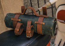 Rolled green and brown leather motorcycle tool roll with brass buckles on vintage scooter seat, handcrafted biker tool bag