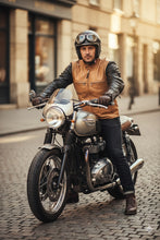 Man wearing tan and black leather café racer jacket riding vintage motorcycle