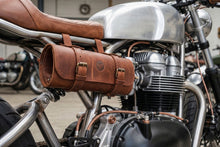 Vintage brown leather motorcycle tool roll securely mounted to the side frame of a custom café racer, featuring buckle straps, durable full-grain leather, and classic styling for motorcycle tool storage and touring