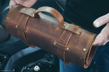 Rear view of a handcrafted leather motorcycle tool roll with reinforced carry handle and secure mounting straps, designed for portable storage and transport of motorcycle repair tools.